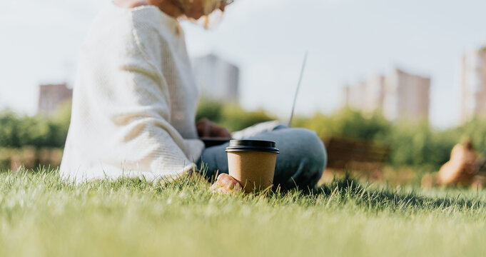 Close Up Coffe Cup. Adult Woman Typing At Laptop And Mobile Cell Phone Outside In Park. Thinking Senior Working And Drinking Coffee. Using Computer. Distance Learning Online Education And Shops.