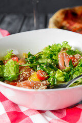 Fresh salad with salmon and vegetables close up in a bowl served with a glass of white wine.