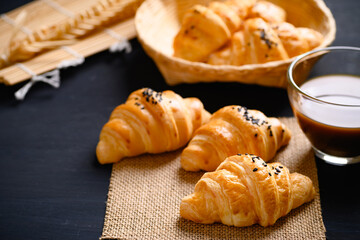 French croissant with black sesame seeds and coffee cup on black background, morning breakfast