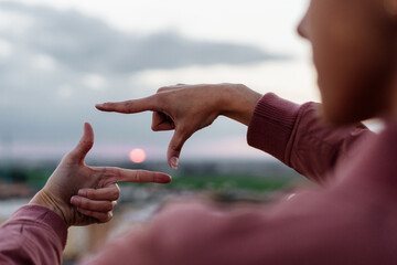 Close-up of woman framing sunset with fingers