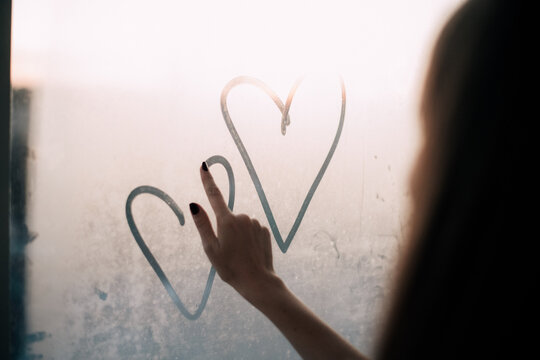 Young woman drawing hearts on the window