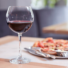 Wine glass filled with red wine on a wooden table with blurred background in restaurant.