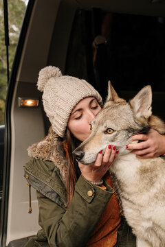 Young woman in camper van petting a cute  wolf dog in the mountain