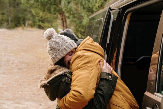 Young couple hugging next to camper van in forest