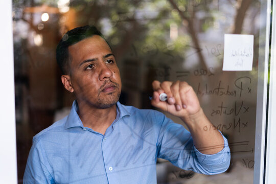 Latin hispanic man working at home and writting graphs on glass wall