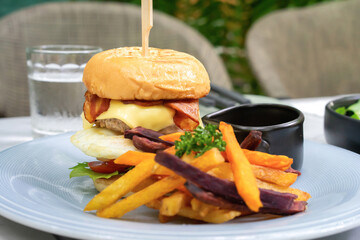 Burger homemade on the white dish with Bacon and Cheese is served with purple Sweet Potato fried in restaurant, Fresh American Food.