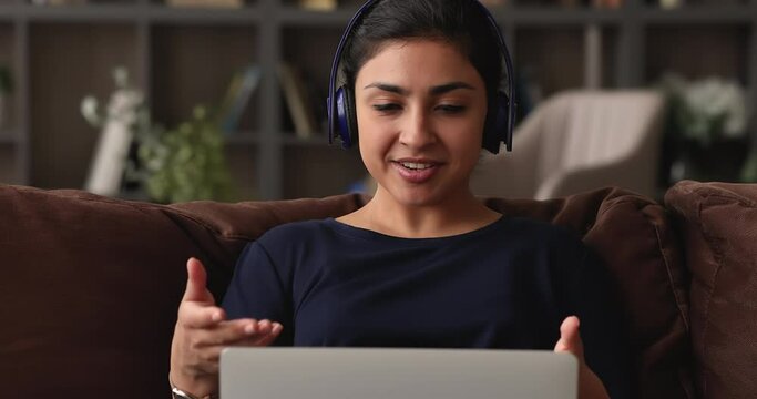 Indian professional counsellor work from home sit on sofa use laptop wear headphones talk to client by videocall, give professional aid in resolving personal psychological problems. Video call concept