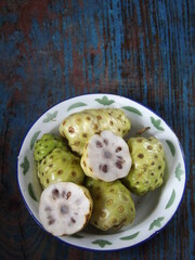 Morinda citrifolia or noni fruit is also known as mengkudu in Indonesia. Popular to used as traditional medicine. Has strong smell and bitter taste. Served on enamel plate. Isolated and copy space.