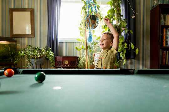 Boy at pool table raises fist in victory