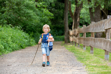 Little toddler boy, walking on little path next to a fence in the park, hiking