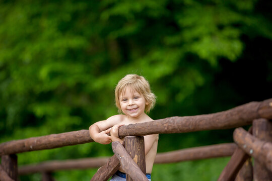 Cute little toddler child, boy, standing on a fence in the park, shirtless