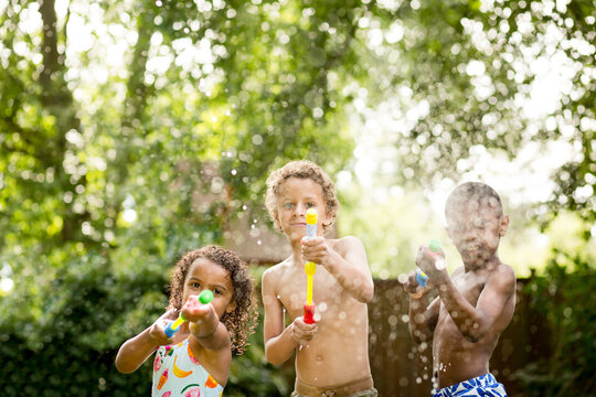 Three children spray water guns into air