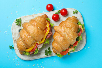 Concept of tasty eating with croissant sandwiches on blue background, top view