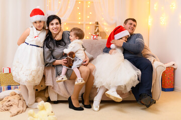 happy big family portrait - parents and children in home interior decorated with holiday lights and gifts, dressed in santa hat for new year celebration