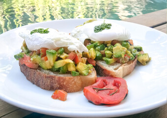 Fresh avocado and poached eggs on homemade bread toasts for healthy low-calorie lunch by the pool in Baliu. 