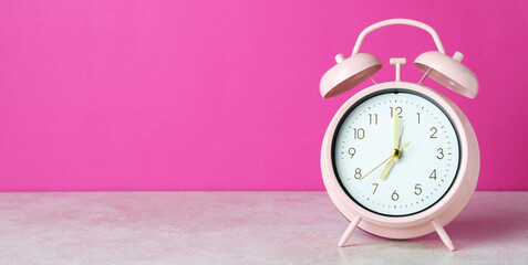 Alarm clock on white textured table against pink background