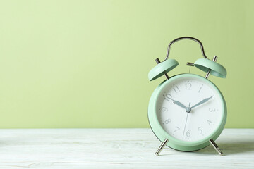 Alarm clock on white wooden table against green background