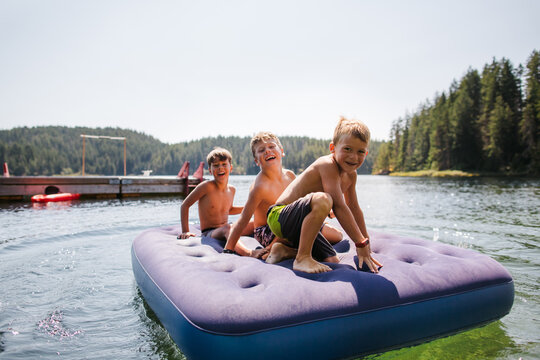 Kids playing on air matress floaty on lake in summer.