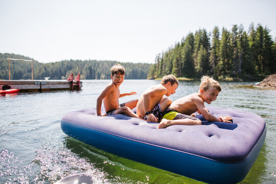 Kids Playing On Air Matress Floaty On Lake In Summer.