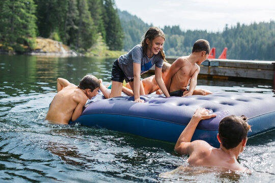 Kids Playing On Air Matress Floaty On Lake In Summer.