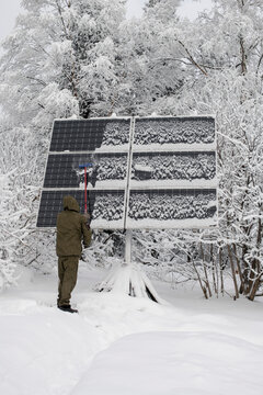 A man pushing snow off solar panels in winter