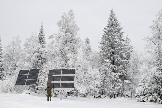 A man pushing snow off solar panels in winter