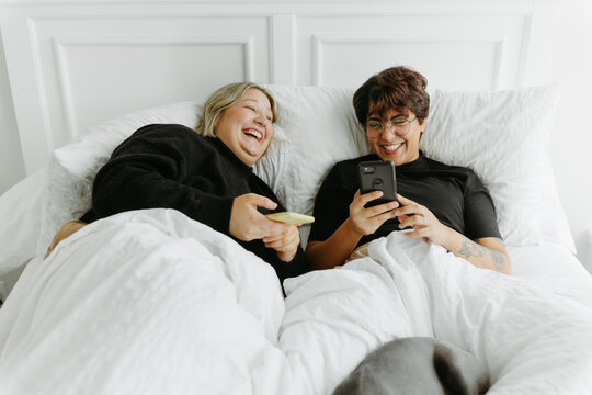 Married couple laying in bed together on phones