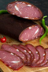 Turkish pastrami on a wooden serving plate. Whole and sliced pastrami. pastrami is made from the ribeye and beef fillet parts of the cow. Close up.