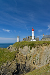 Fototapeta na wymiar vue sur falaise de granit avec le phare blanc et rouge de la pointe Saint Mathieu et son Abbaye du Finistère en ruine sous un ciel bleu de Bretagne 