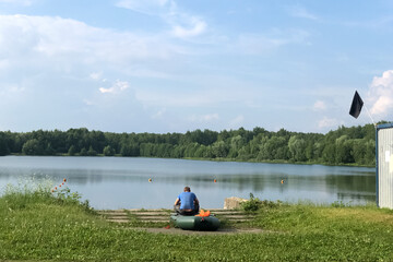 Man sits on board an inflatable boat on the lake shore on a summer day