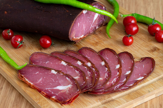 Turkish pastrami on a wooden serving plate. Whole and sliced pastrami. pastrami is made from the ribeye and beef fillet parts of the cow. Close up.