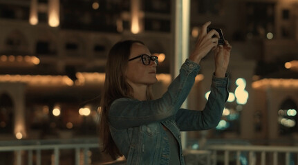 Woman work on smart phone in city at night time over business tower. Blured bokeh background.