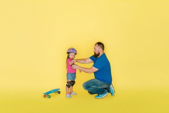 Dad helps young daughter with elbow pads