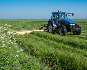tractor in meadow with summer flowers mowing grass under blue sky in holland