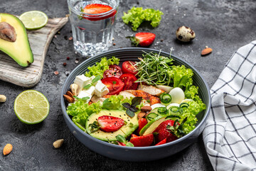 Fototapeta na wymiar Healthy buddha bowl lunch with grilled chicken and avocado, feta cheese, quail eggs, strawberries, nuts and lettuce. Delicious balanced food concept