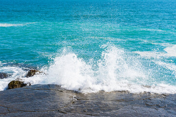 Fototapeta premium White wave of the turquoise sea breaks on a stone on the shore on a bright sunny day