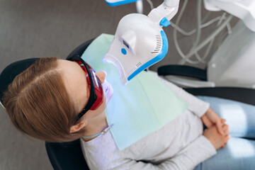 Attractive woman in a dental chair with goggles on a visit to the dentist. Work equipment shines on the patient's teeth