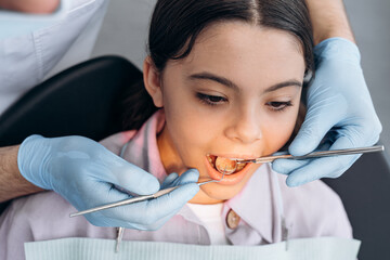 Close-up view, the dentist examines the teeth of a little girl with the help of dental instruments. Concept of taking care of dental health