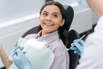 Positive, cheerful teenage girl smiling at the dentist. The doctor tells the patient how to treat the teeth.