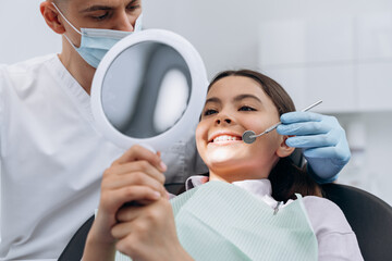 Cute, attractive girl on a visit to the dentist holding a mirror. The doctor examines the patient's teeth