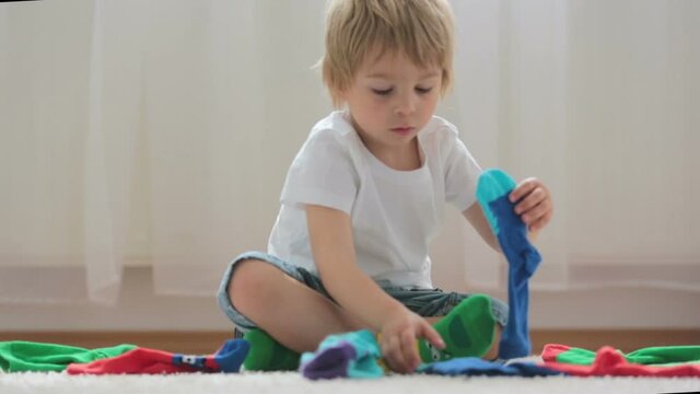 Child, toddler boy, pairing different colorful socks, sitting on the floor