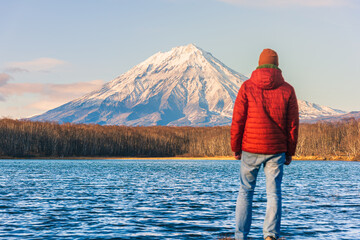 A man dressed in red looks at a majestic volcano on Russia's famed Kamchatka Peninsula. Inspiring pictures of travel.