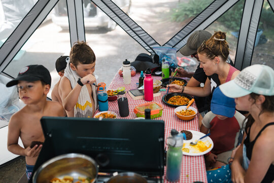 Kids and parents eating food in picnin table shelter while campi