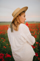 Young beautiful woman wearing white linen suit and straw hat posing in a poppy field.