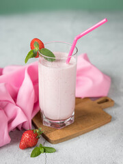 Strawberry smoothie with milk in a glass  on a white  background .  Homemade strawberry milk shake in a glass  with a mint leaves  and strawberry berries on a pink napkin . 