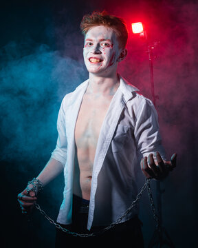 Portrait of a maniac with blood on his face and chain in his hands against a background of red and blue smoke