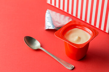 Yogurt cup on red background - single pot of fruit yoghurt in red plastic container, foil lid and...