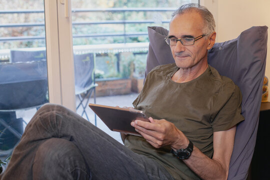 senior elderly man using digital tablet computer at home, watching video or reading