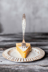 Slice of lemon pie on white ceramic plate, grey wooden background, selective focus, copy space