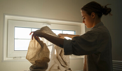 Young woman drying linen against window